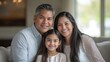 © CStock - A father, mother, and daughter posing for a portrait at home, with the daughter sitting on her father lap and the mother standing beside them Close-up photo with clean background