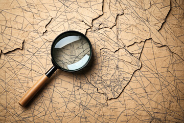 Poster - Vintage-style map with black lines and text on brown paper, partially torn. A magnifying glass with a wooden handle lies on top, magnifying part of the map.