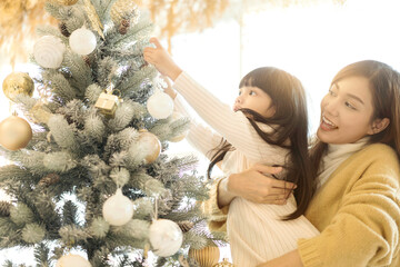 Merry Christmas and Happy New Year! Little daughter helping her mother decorate the christmas tree with christmas ball. Gold color tone.