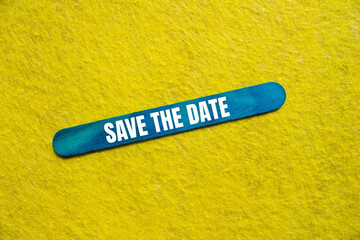 Save the date message written on blue wooden stick with yellow background. Conceptual save the date symbol. Copy space.