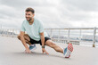 © muse studio - A Man Performing a Dynamic Stretching Exercise Outdoors on a Cloudy Day Near a Waterfront