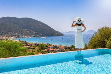 Summer travel concept with a beautiful luxury woman enjoying the panoramic view of the mediterranean sea from the swimming pool