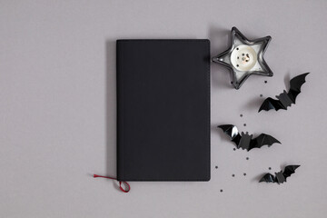 Happy Halloween holiday concept. Black notebook cover Halloween decorations burning candles stars bats Halloween party on gray background. Halloween greeting card mockup  copy space. Flat lay top view