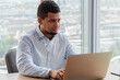 © maxximmm - Man is working on his laptop at desk. office technology computer concept. man is sitting at table with laptop. a man is sitting at a desk with a laptop and a lifestyle table for business.