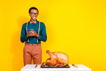 Wall Mural - Portrait of elegant young man hold phone look roasted thanksgiving day turkey empty space isolated on yellow color background