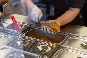 Worker preparing Mexican tacos on food counter in fast food restaurant