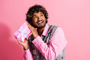 Poster - Photo of nice young man hold giftbox look empty space wear christmas vest isolated on pink color background