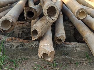 A close-up of a stack of weathered bamboo poles, showing the natural texture and hollow interior of the culms.