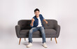 © STOCK88PHOTOGRAPHER - Full body image of young Asian man posing on sofa on white background