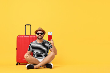 Canvas Print - Happy man in sunglasses with passport, tickets and suitcase on orange background, space for text