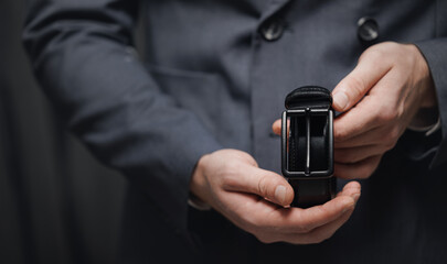 closeup hand of men hold leather belt for classic suit, dark background