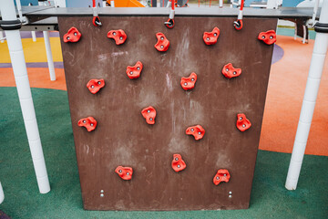 In a cheerful, lively playground, a vibrant climbing wall adorned with bright red holds captivates children, promoting fitness, social interaction, and essential life skills through play