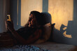 © Luis Herrera/Stocksy - young woman in bed with phone in dark room at dawn