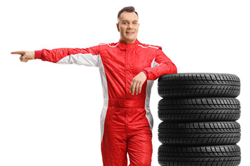 Car racer leaning on a pile of tires and pointing to the side