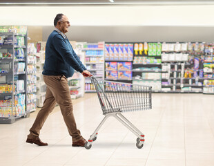 Wall Mural - Full length profile shot of a mature man walking and pushing an empty shopping cart