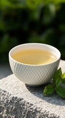 Sticker - Cup of white tea resting on a stone surface with a sprig of fresh mint beside, simple and refreshing tea experience 