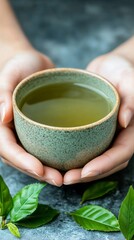 Canvas Print - Hands holding a ceramic cup of green tea, with fresh leaves scattered on the table, peaceful and natural tea moment 