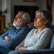 © Tadeusz - Sad mature couple with gray hair sitting on a couch, looking pensive and distant.