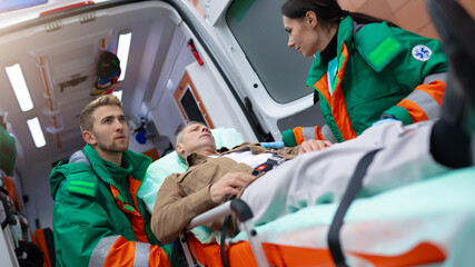 paramedics in green and orange uniforms attend to a male patient on a stretcher, preparing him for t