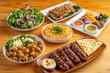 © serdon - Grilled lamb kebabs, chicken skewers with roast vegetables, and appetizers variety served on wooden outdoor table in Middle Eastern, Arabic, or Mediterranean style.