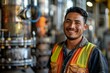 © Vera - Portrait of a young Hispanic factory worker technician in safety uniform smiling in front of industrial machinery.
