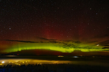 a vivid aurora borealis with striking red and green hues lights up the starry night sky above a town