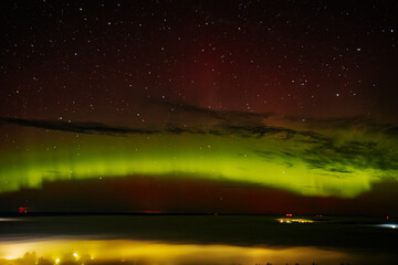 a vivid aurora borealis with striking red and green hues lights up the starry night sky above a town