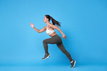 Wall Mural - Woman in sportswear running on light blue background