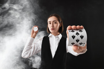 Canvas Print - Croupier holding cards and dealer button on black background with smoke, selective focus