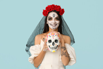 Wall Mural - Young woman dressed as dead bride for Halloween party with painted human skull on blue background