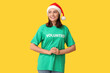© Pixel-Shot - Beautiful female volunteer in Santa hat on yellow background