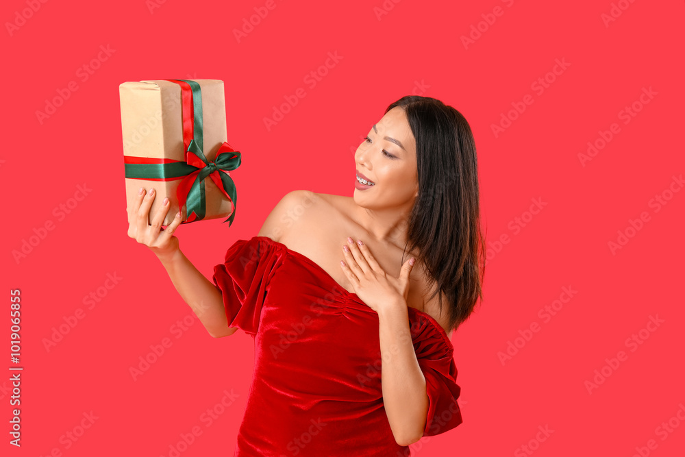 Young Asian woman with Christmas gift box on red background