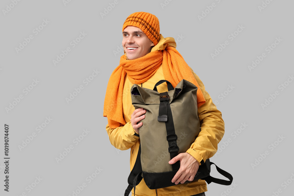 Young man in yellow stylish jacket and scarf with bag on grey background