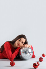 Poster - Beautiful young woman with Christmas decorations and disco ball lying on grey background