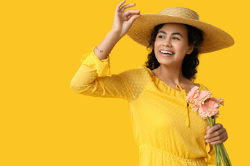 Wall Mural - Beautiful young African-American woman with bouquet of gerbera flowers on yellow background. International Women's Day