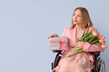 Wall Mural - Young woman in wheelchair with tulips and gift on blue background. International Women's Day