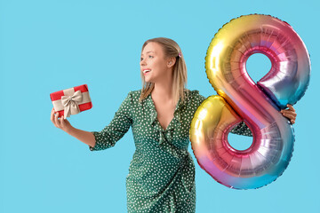 Canvas Print - Young woman with hearing aid holding balloon in shape of figure 8 and gift on blue background. International Women's Day