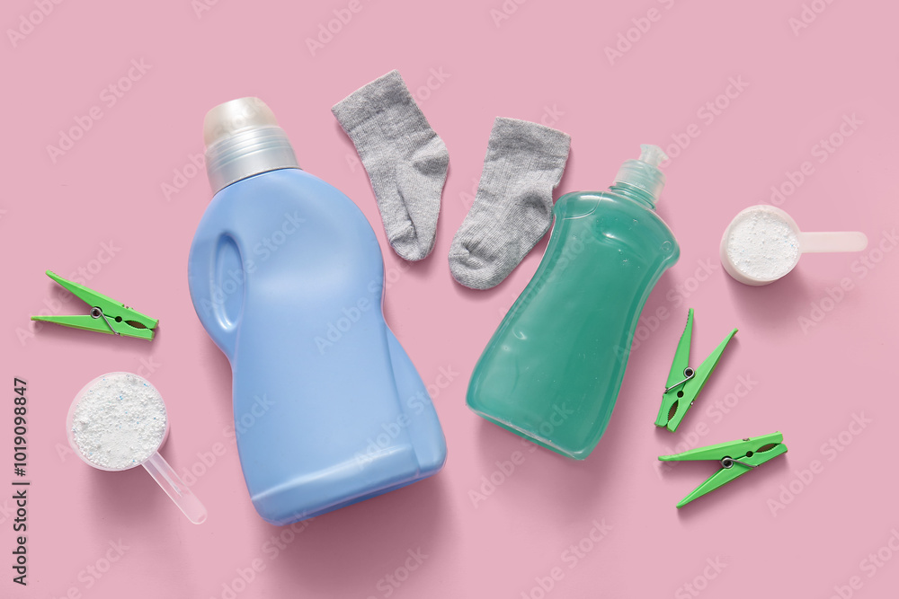 Laundry detergents with clothespins and baby socks on pink background