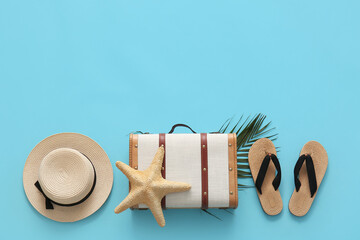 Suitcase with starfish, leaf and beach accessories on blue background