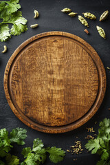 Wall Mural - An empty wooden round board surrounded by dried fennel seeds, cardamom pods, and fresh cilantro leaves on a deep black background, ideal for a menuâ€™s top-view layout.