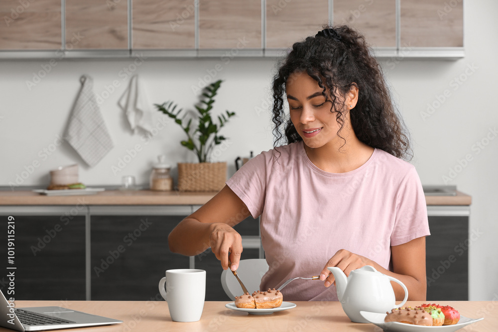 African-American woman eating tasty eclair in kitchen