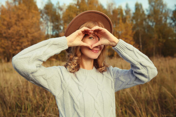 Wall Mural - Beauty portrait of stylish happy young woman showing heart gesture, girl smiling in autumn park