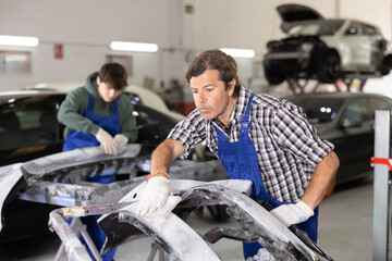 Adult male mechanic in uniform polishes part of car with sponge in car service station