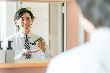 朝洗面所でスキンケア・フェイスケアするスーツ姿の男性（乳液・クリーム・保湿・身じたく・肌ケア）
