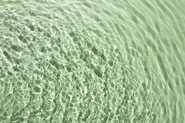 Rippled surface of clear water on light green background, top view