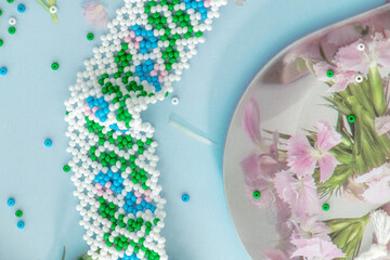 Wall Mural - Close up on beaded necklace made of white, blue and green beads surrounded by carnation flowers