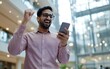 © Mavita - A joyful man celebrates a success while checking his smartphone in a modern, well-lit indoor space.