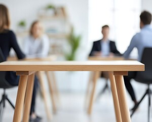 Focused view of a wooden table in a modern office with blurred people in background.