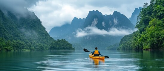 Wall Mural - man kayaking on a serene lake surrounded by lush green mountains and fog.