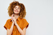 © SHOTPRIME STUDIO - Smiling woman with curly hair in an orange shirt on a plain light background, conveying happiness and positivity, ideal for lifestyle and fashion themes